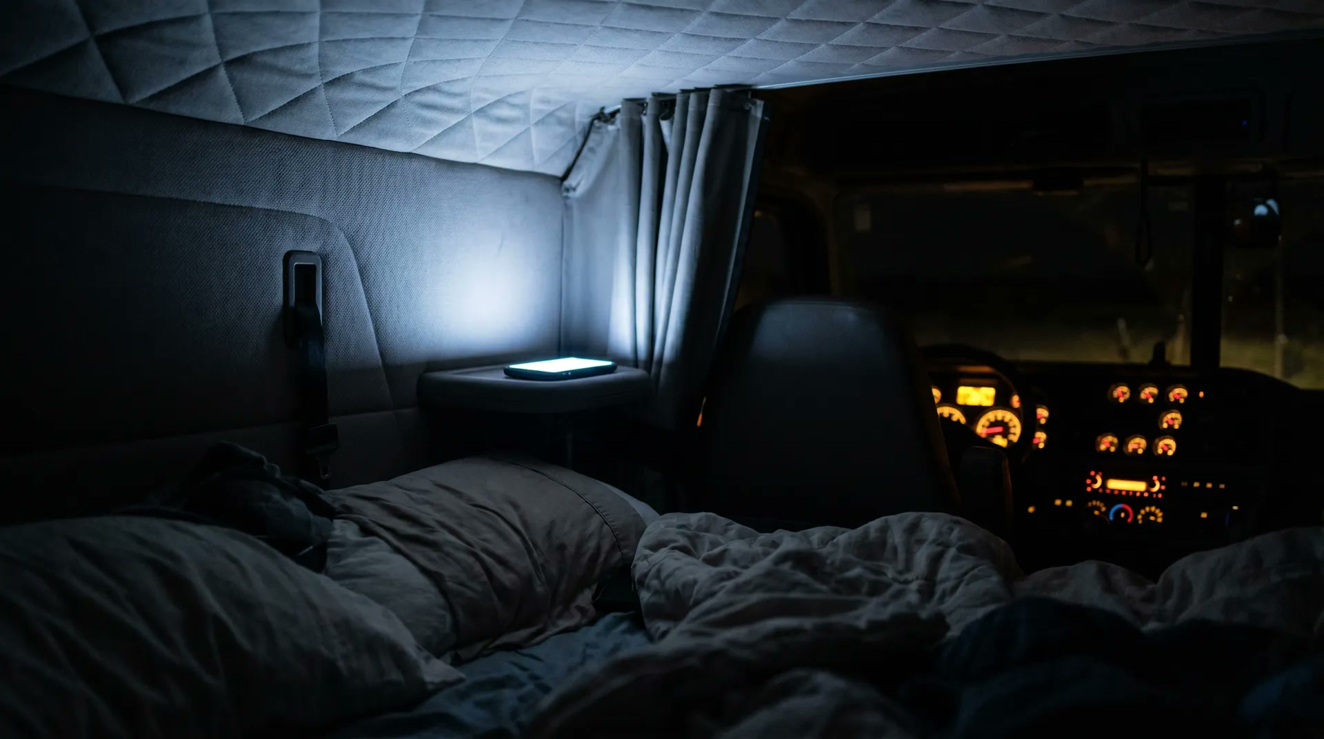 Phone screen glowing inside a dark sleeper cab at night